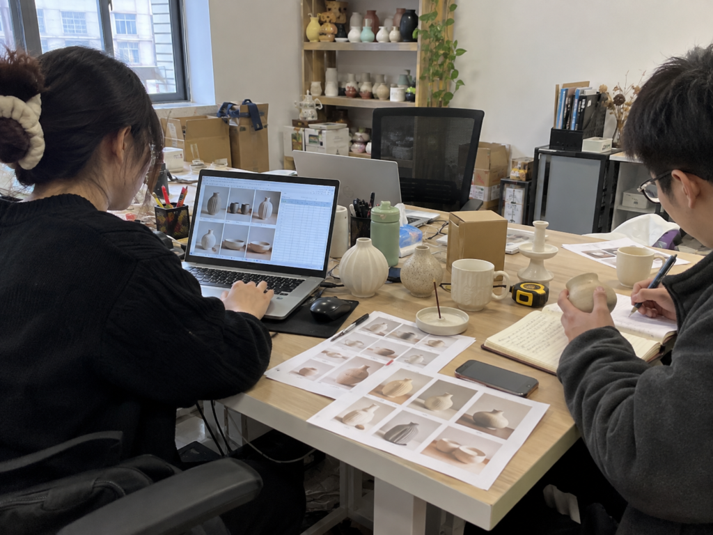 Illustrative ceramic sourcing office scene showing product coordination, laptop work and ceramic samples